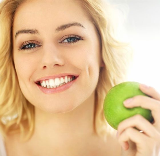 Women With White Teeth Holding A Green Apple — Suncoastdental In Maroochydore, QLD